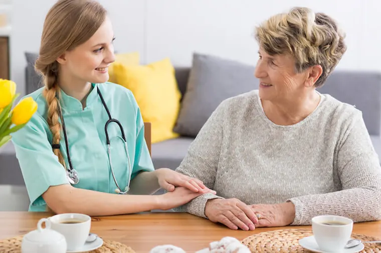 Carer and older woman having tea at the kitchen table
