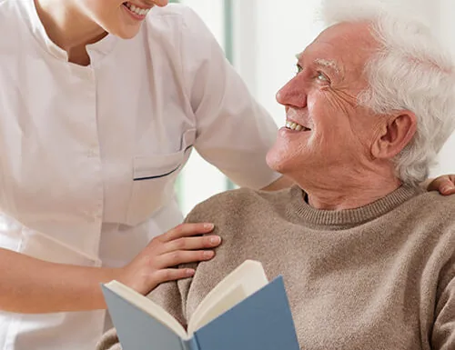 Carer reading with an older man in his chair