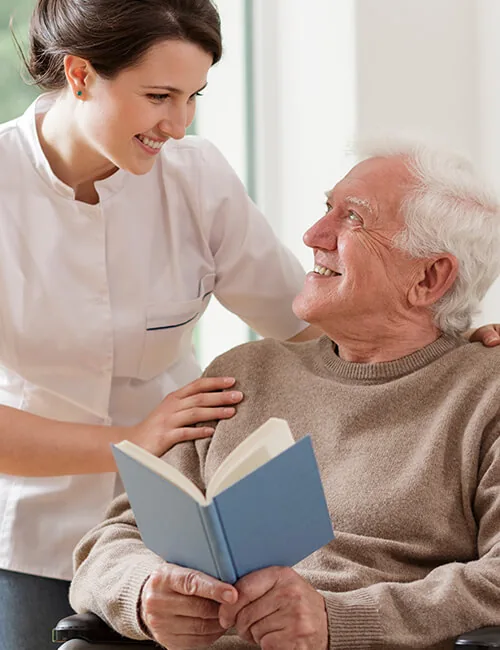 Carer reading with an older man in his chair