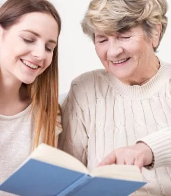 Carer reading a book with an older woman