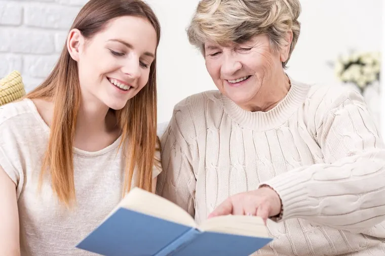 Carer reading a book with an older woman