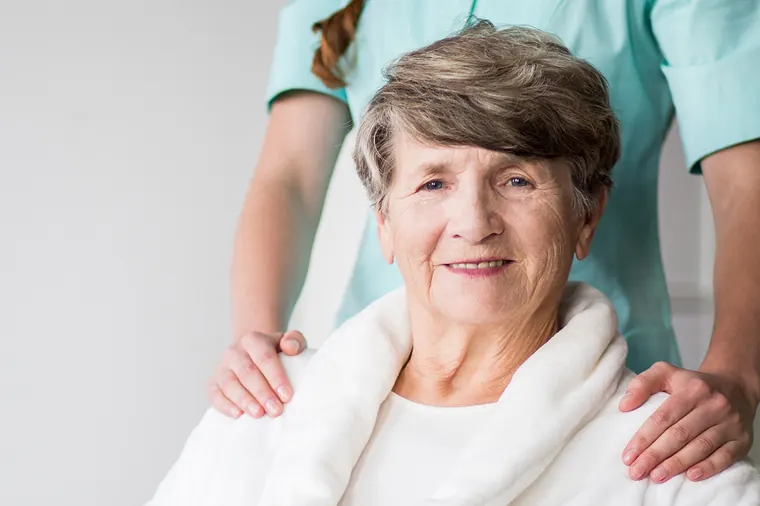 Smiling older woman with a carer behind her